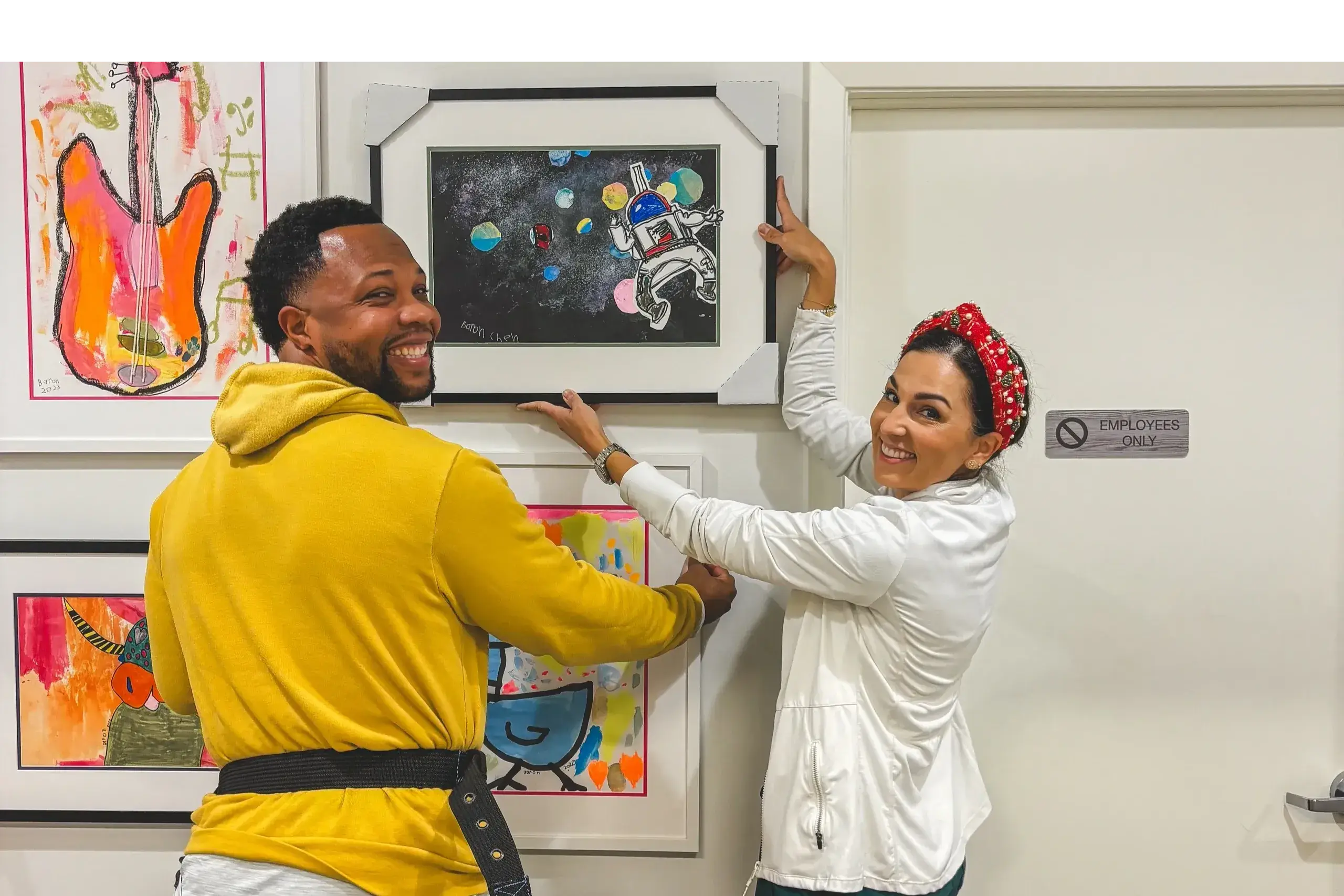 Two people are hanging a picture on the wall.